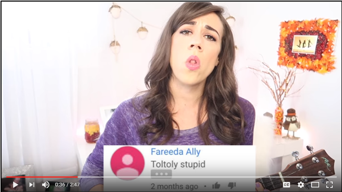 Colleen Ballinger sings “Toltoly stupid” while rolling her tongue to emphasize the misspelling. A screencap of the comment appears below her.