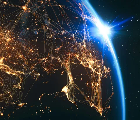A view of Earth from space at night showing Europe and surrounding regions illuminated by city lights connected by glowing network lines, with a bright sunrise on the horizon.