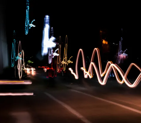 Long-exposure photograph of city lights at night creating swirling, wave-like trails of white, blue, red, and yellow against a dark background.