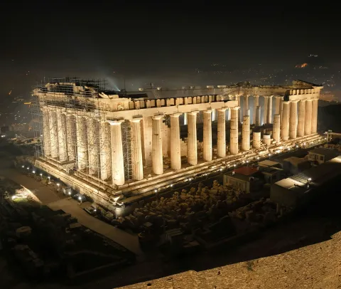 Illuminated ancient temple with columns at night, overlooking a city.