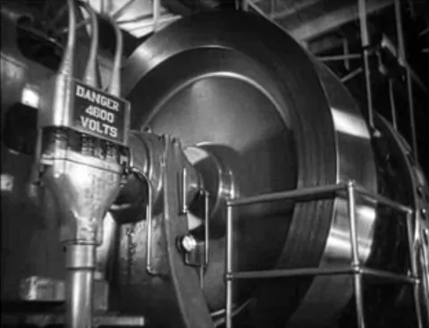 Black-and-white photograph of a large industrial generator or turbine with metal piping and a warning sign reading "Danger 4800 Volts."