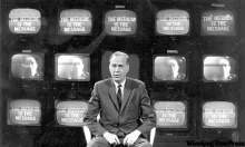 Marshall McLuhan sit in front of several screen, black and white photo