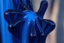 Abstract close-up of glossy blue glass form with smooth curves and reflective surface.