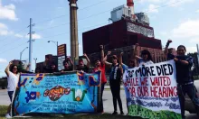 A group of environmental justice activists raising fists in front of an industrial power plant, holding banners for the Little Village Environmental Justice Organization and one reading "30 More Died While We Waited for Our Hearing."