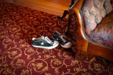 A pair of shoes sits on an ornate carpet near a couch.