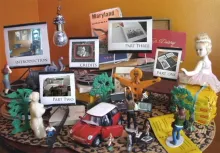 A tabletop diorama with miniature figures, toy cars, trees, a doll, and film reels arranged around labeled photo cards reading "Introduction," "Credits," "Part One," "Part Two," and "Part Three."