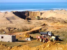 dump trucks are on a beach by the ocean engaged in Illegal beach sand mining on the Moroccan coast. 