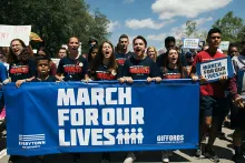 students in a protest march hold up a March for our Lives sign